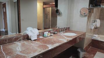 A bathroom with a marble vanity, a large mirror, a sink, a shower, and a toilet.