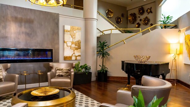 Een ruime woonkamer met een modern design, met een ronde salontafel, comfortabele zitplaatsen, een vleugelpiano en een trap met een gouden leuning.