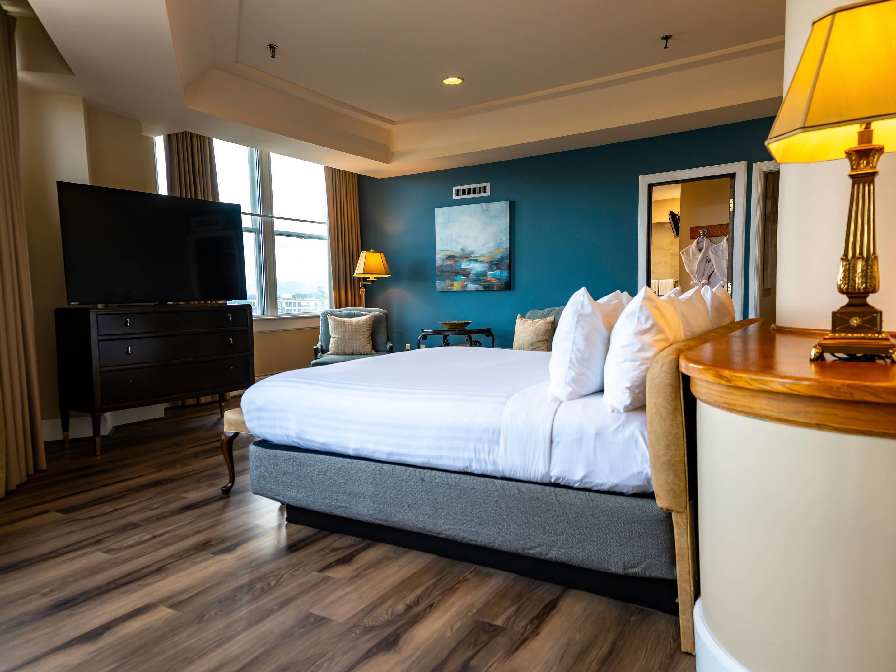 A hotel room with a large bed, a flat-screen TV, a desk with a lamp, and a painting on the wall.