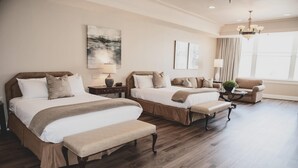 Een hotelkamer met twee bedden, een bankje, een stoel, een lamp en een raam met gordijnen.