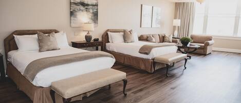 Habitación de hotel con dos camas, un banco, una silla, una lámpara y un ventanal con cortinas.