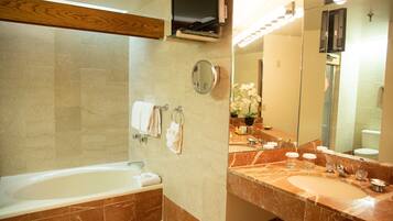 Un baño moderno con una bañera, un lavamanos con lavabo, un espejo y un televisor sobre la bañera.