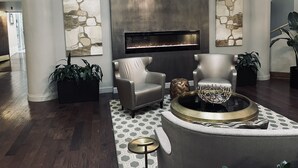 Een moderne lobby met een open haard, leren fauteuils, een ronde salontafel en een kroonluchter.