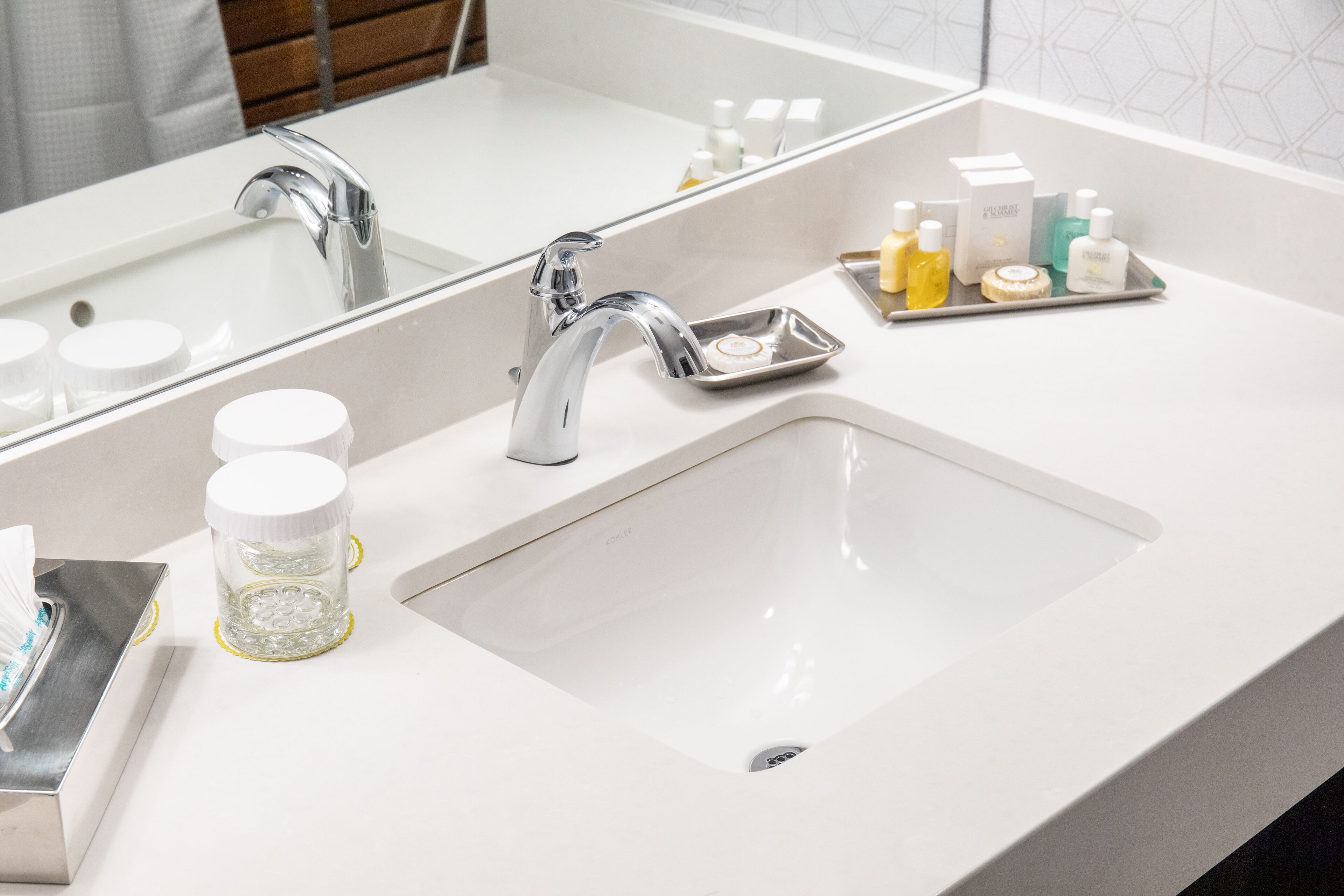 A modern bathroom with a white sink, chrome faucet, and a mirror. There are toiletries on the sink counter.