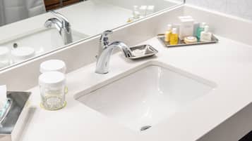 Un baño moderno con un lavabo blanco, grifo cromado y un espejo. Hay artículos de aseo en la encimera.