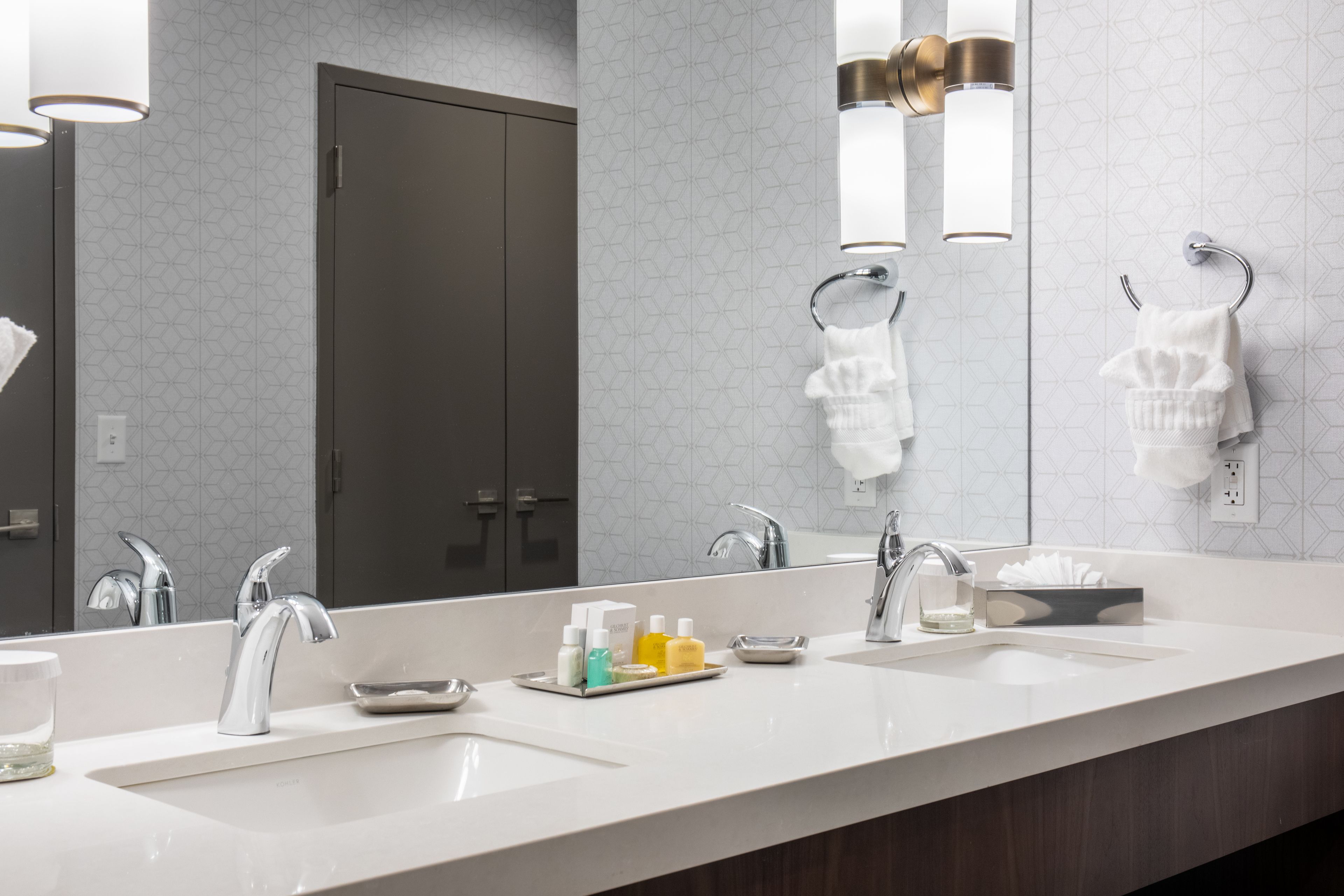 A modern bathroom with two sinks, a large mirror, and a towel rack.