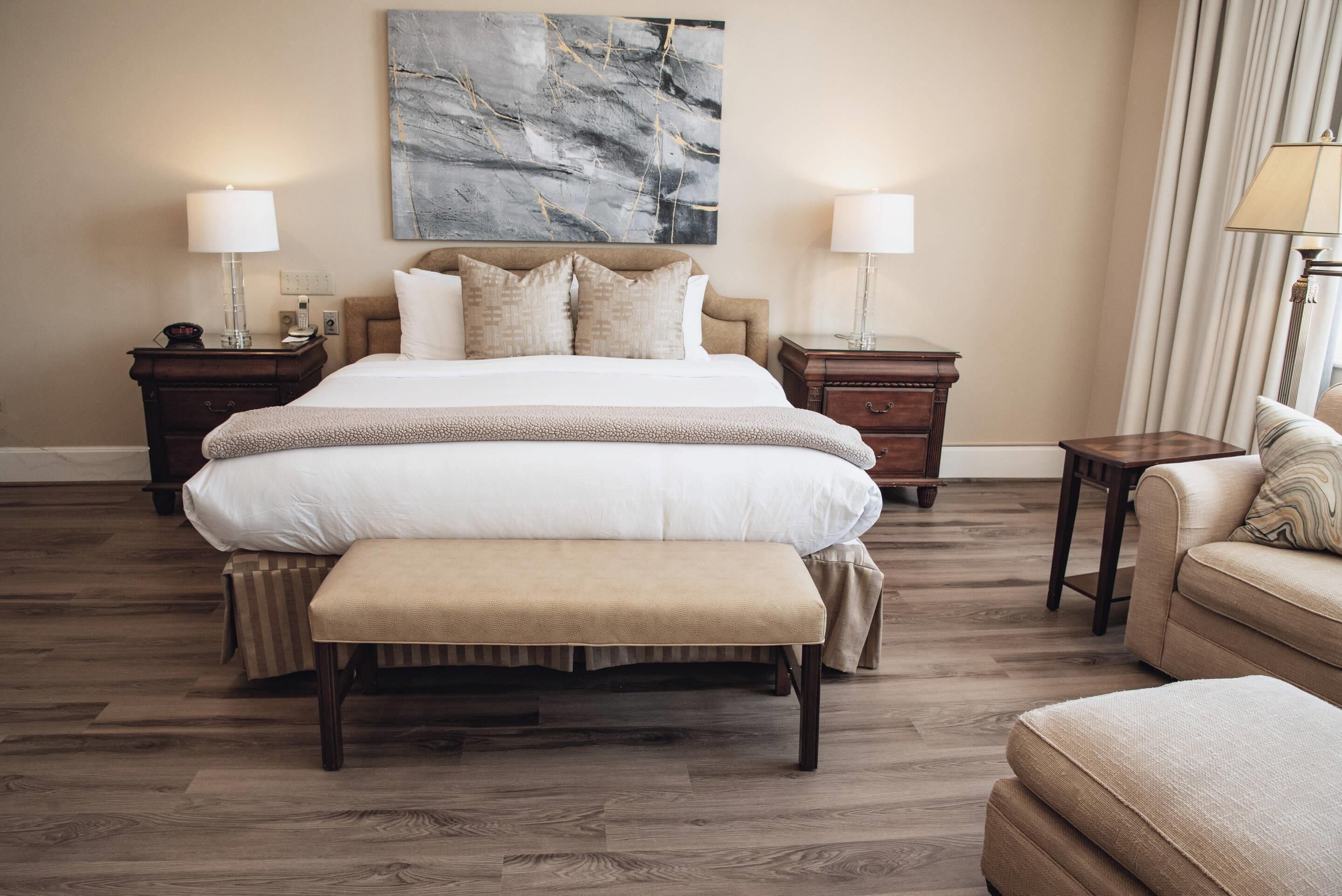 A hotel room with a large bed, two bedside tables with lamps, a bench, and a sofa.
