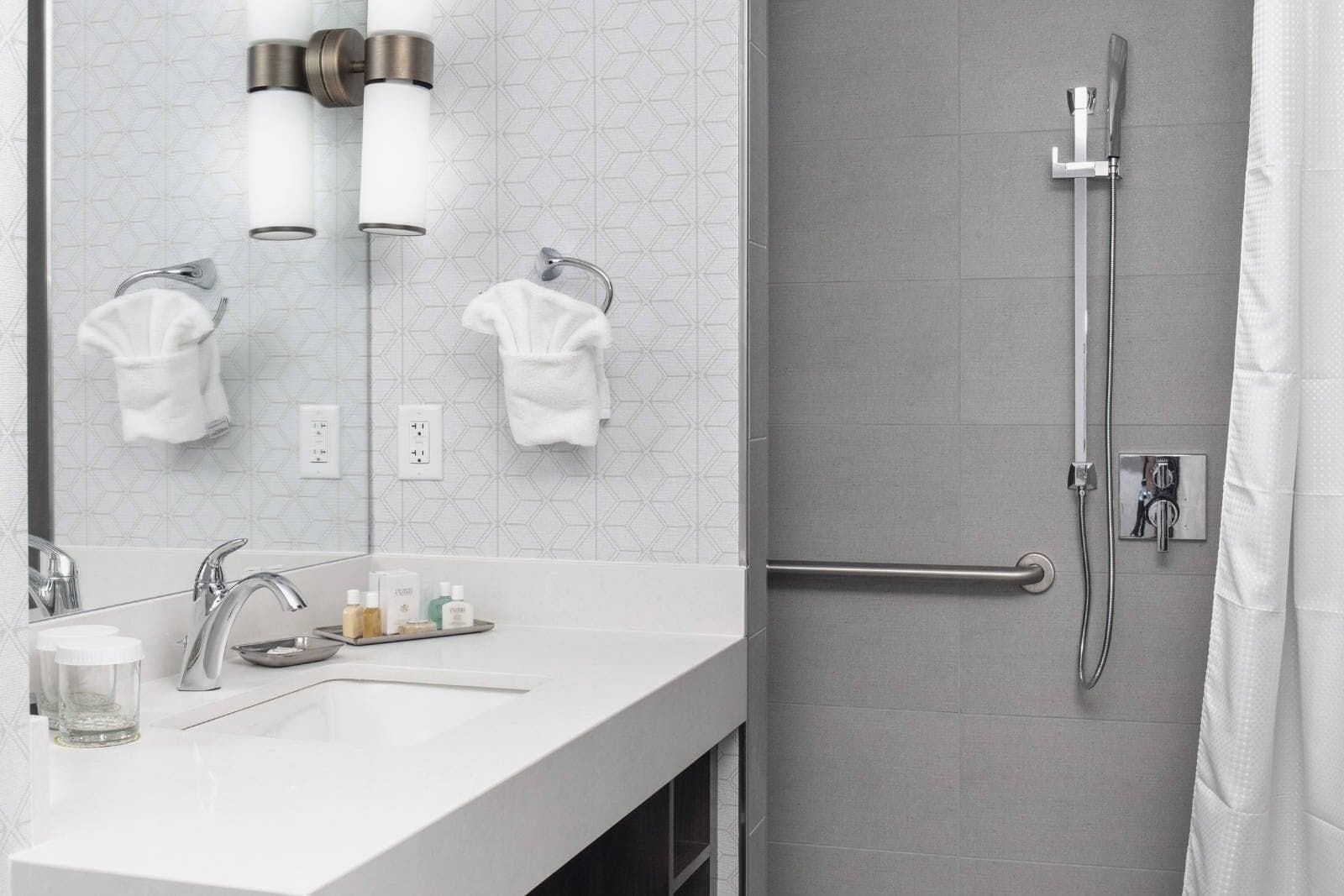 Een moderne badkamer met een douche, een wastafel met toiletartikelen en twee handdoeken aan haken.