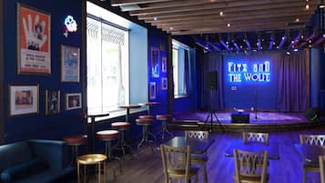Un escenario con un letrero de neón que dice 'Fitz and the Wolf' en una sala con pisos de madera, taburetes de bar y cuadros en las paredes.