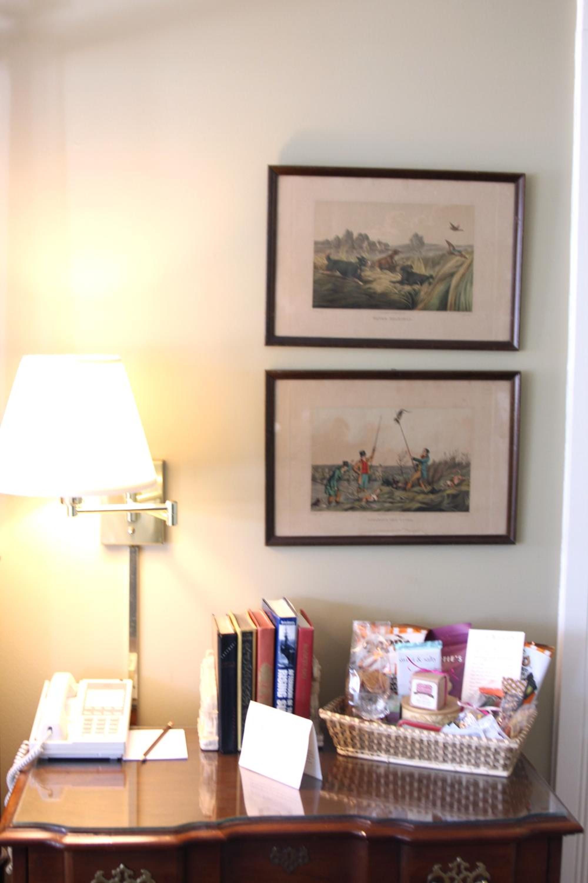 A desk with a lamp, books, a basket of items, and two framed pictures on the wall.