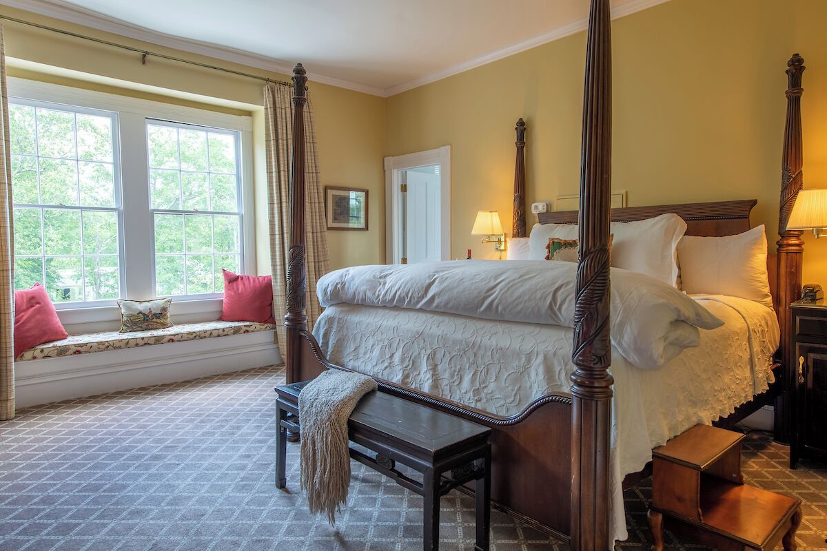 A four-poster bed with a canopy, a bench at the foot of the bed, and a window seat with cushions.