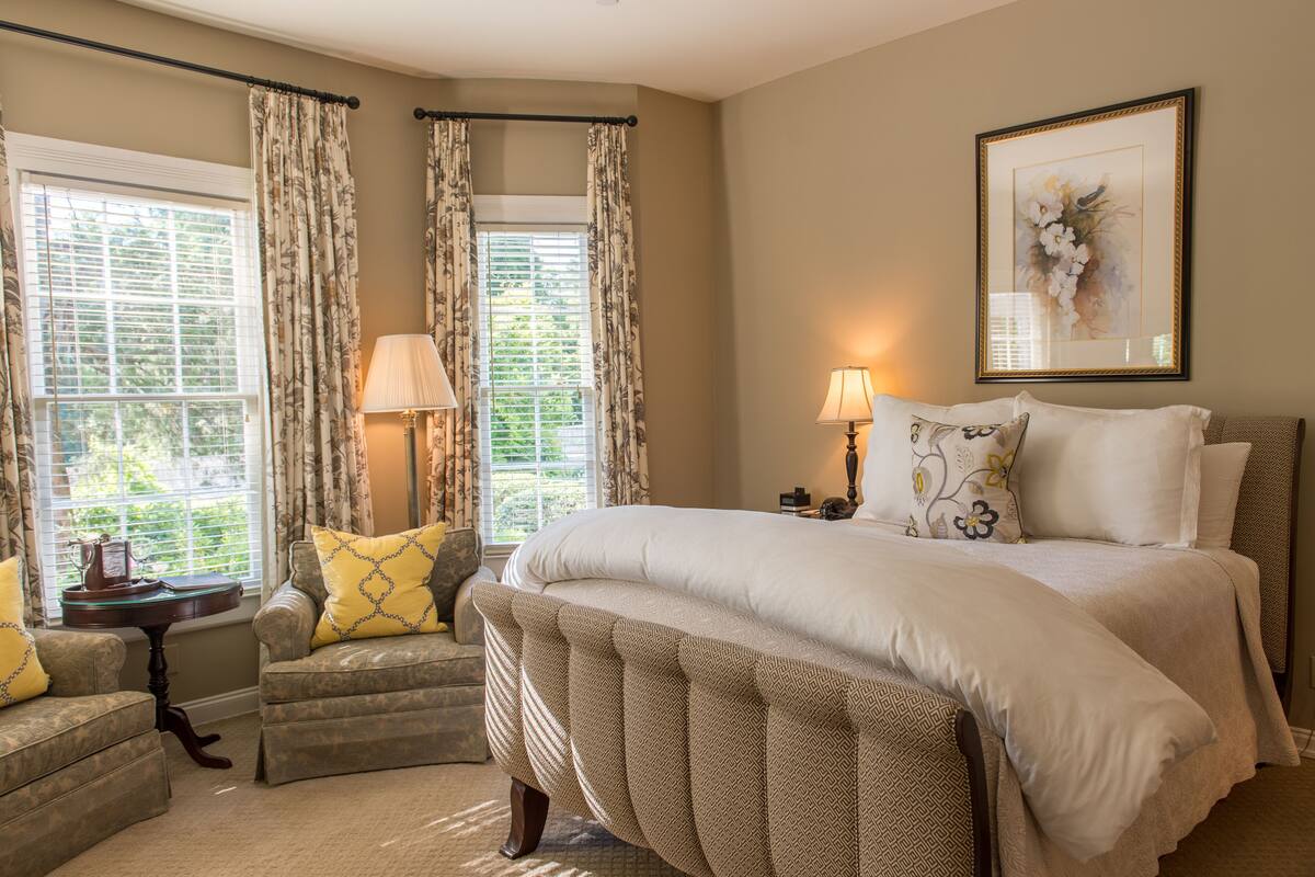 A bedroom with a large bed, two armchairs, a small table, and a lamp.