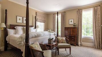 A four-poster bed with a nightstand, a chair, and a wooden cabinet in a room with large windows and a checkered floor.