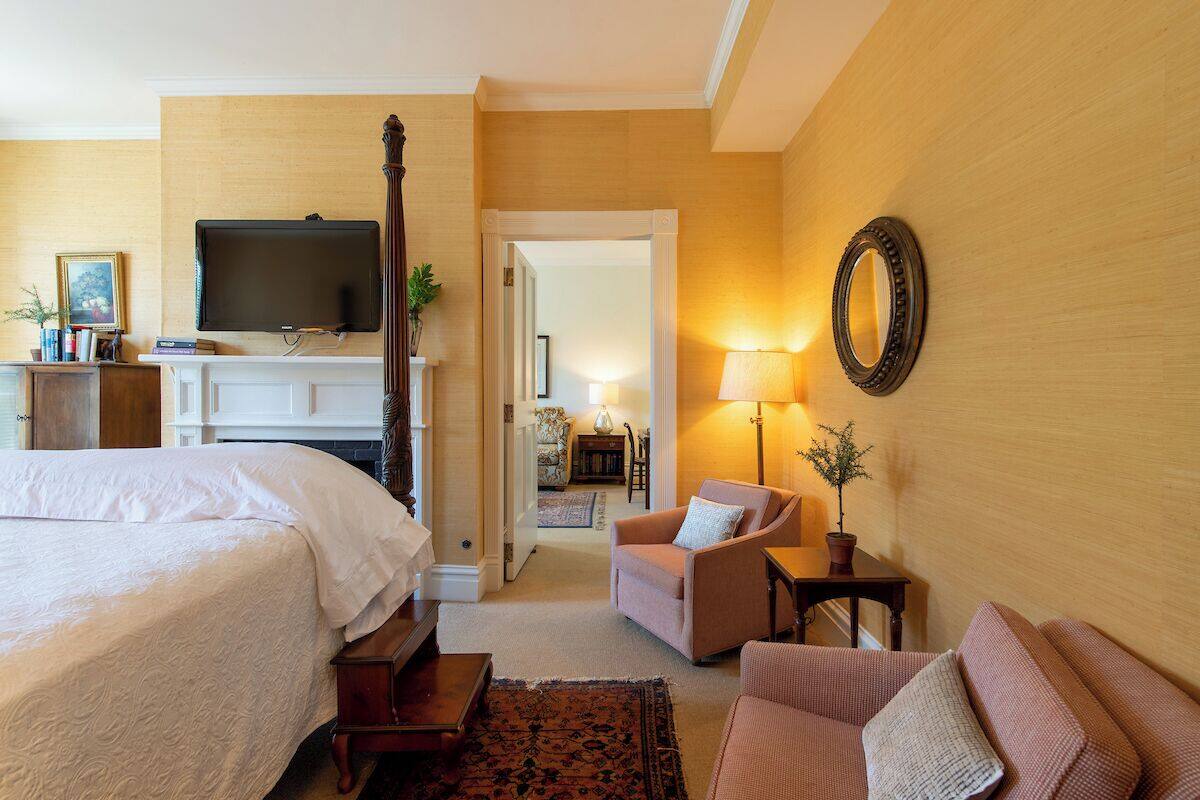 A hotel room with a bed, a television, a chair, a sofa, a lamp, and a mirror.