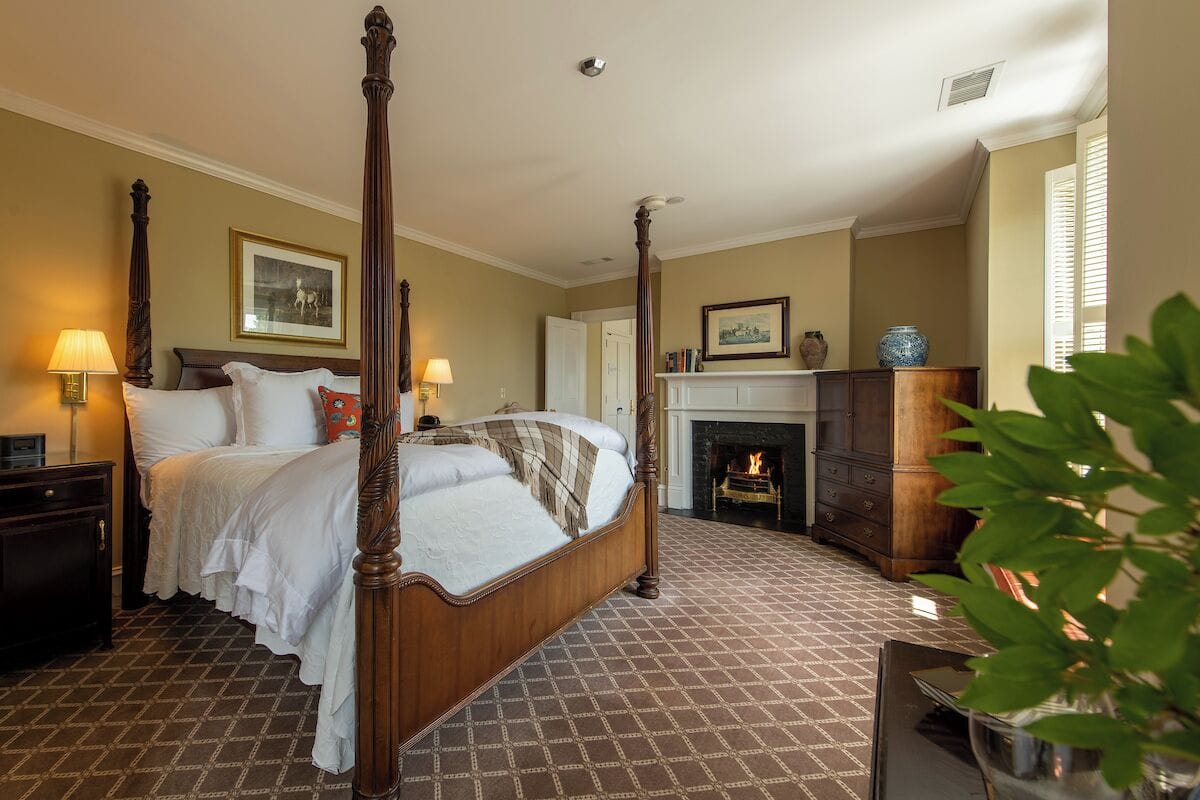 A four-poster bed with a fireplace, a nightstand, and a bedside table.