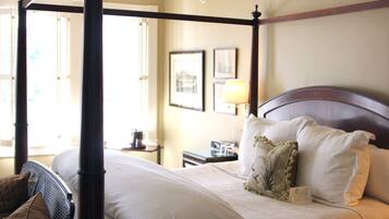 A four-poster bed with white linens, a wooden headboard, and a nightstand with a lamp.