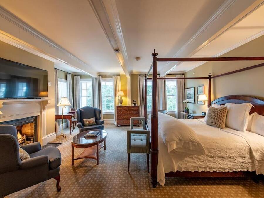 A hotel room with a four-poster bed, a fireplace, a television, and a seating area with a table and chairs.