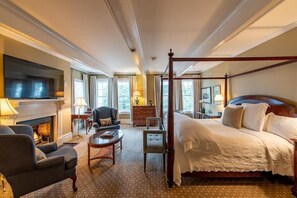 A hotel room with a four-poster bed, a fireplace, a television, and a seating area with a table and chairs. - The Willcox (Aiken)