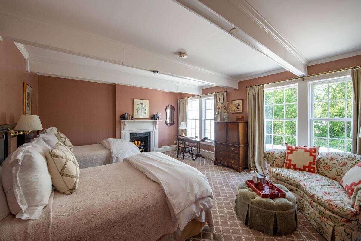 A room with two beds, a sofa, a fireplace, and large windows.
