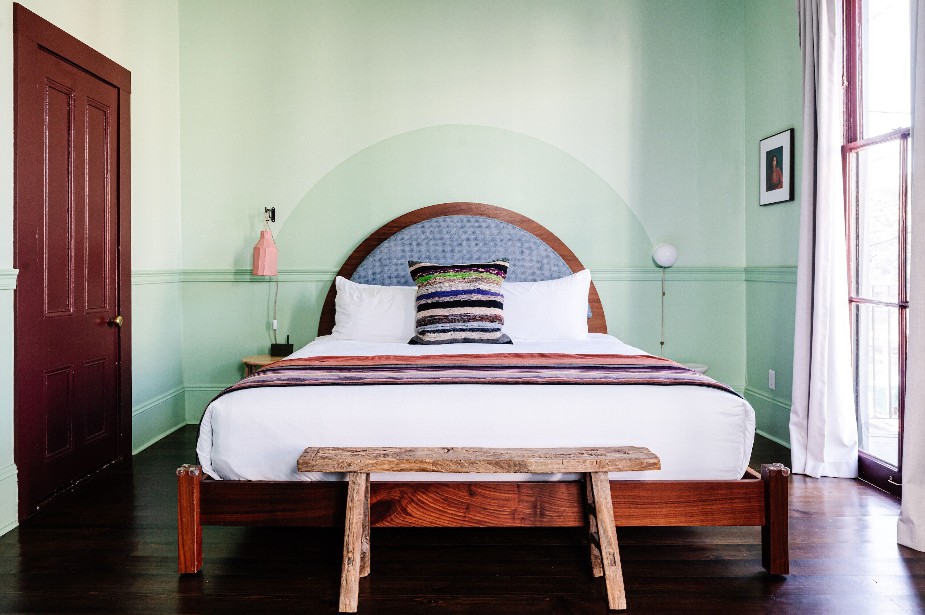 Un lit avec un cadre en bois, un matelas blanc et un oreiller rayé aux couleurs vives.