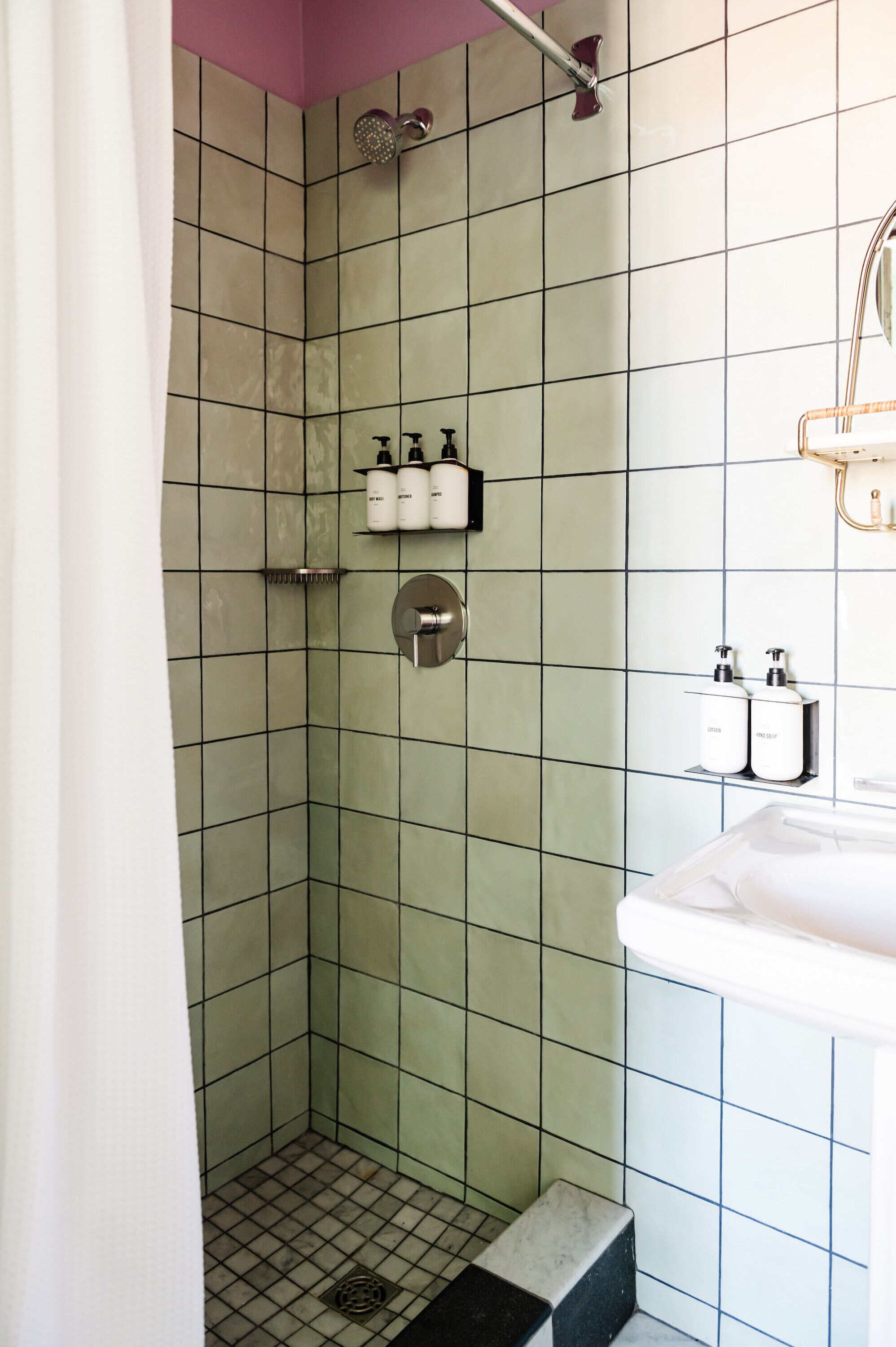 A bathroom with a shower, a sink, and toiletries on shelves.