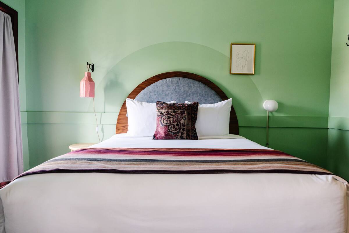 A neatly made bed with a patterned throw, a wooden headboard, and a wall-mounted lamp.