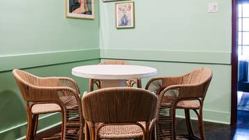 Un comedor con una mesa redonda y cuatro sillas de mimbre, paredes verdes y obras de arte enmarcadas.