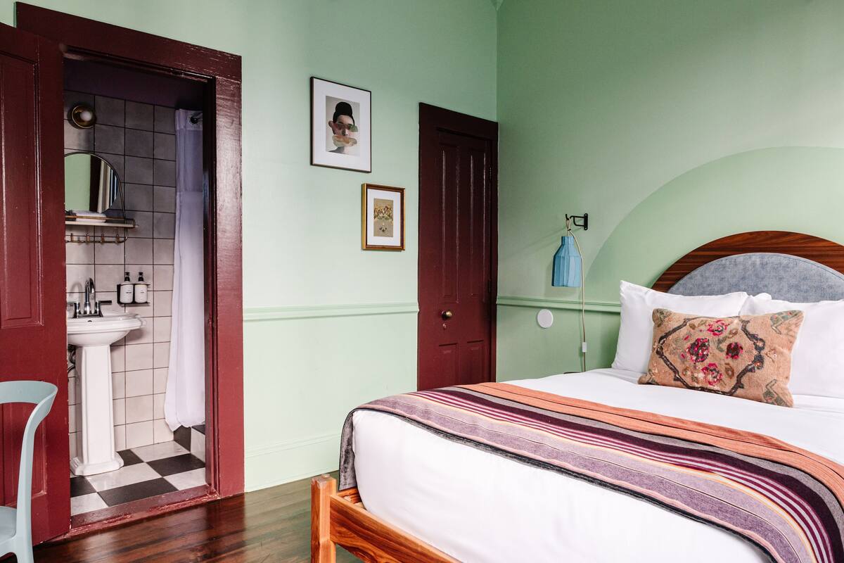 A bedroom with a bed, a wooden headboard, a nightstand, a mirror, a sink, and a door.
