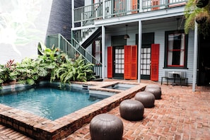 A pool area with a brick border, a staircase, and red shutters on the building. - The Frenchmen New Orleans by Kasa Living (New Orleans)
