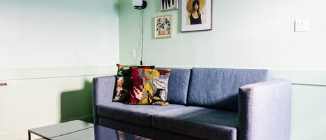 A modern living room with a grey sofa, a glass coffee table, and a red patterned rug.