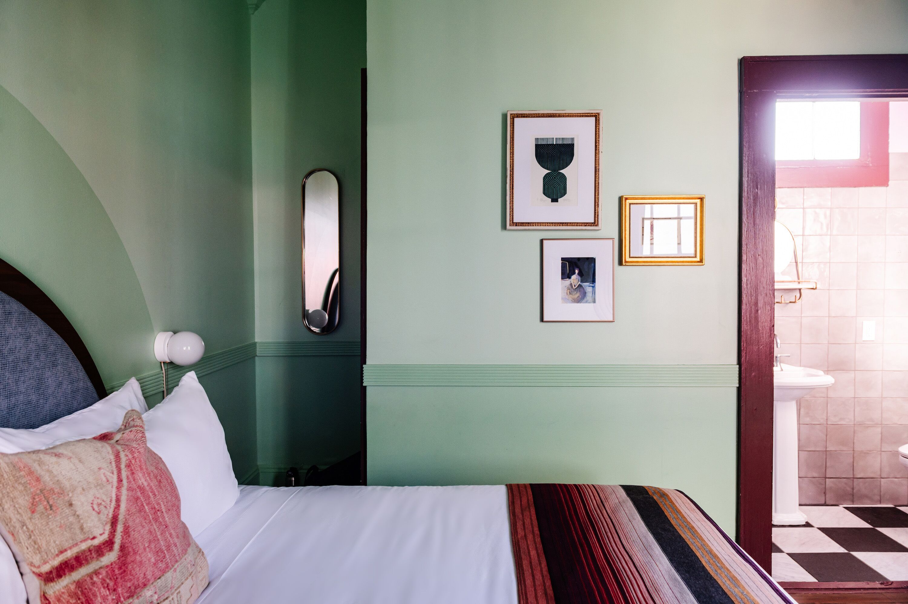 Una habitación de hotel con una cama, una mesita de noche, un espejo y cuadros en la pared.