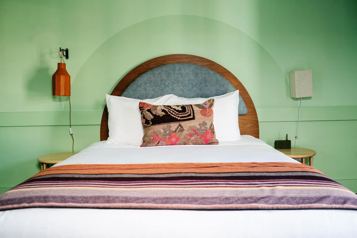 A bed with a wooden headboard, a patterned throw blanket, and a decorative pillow.