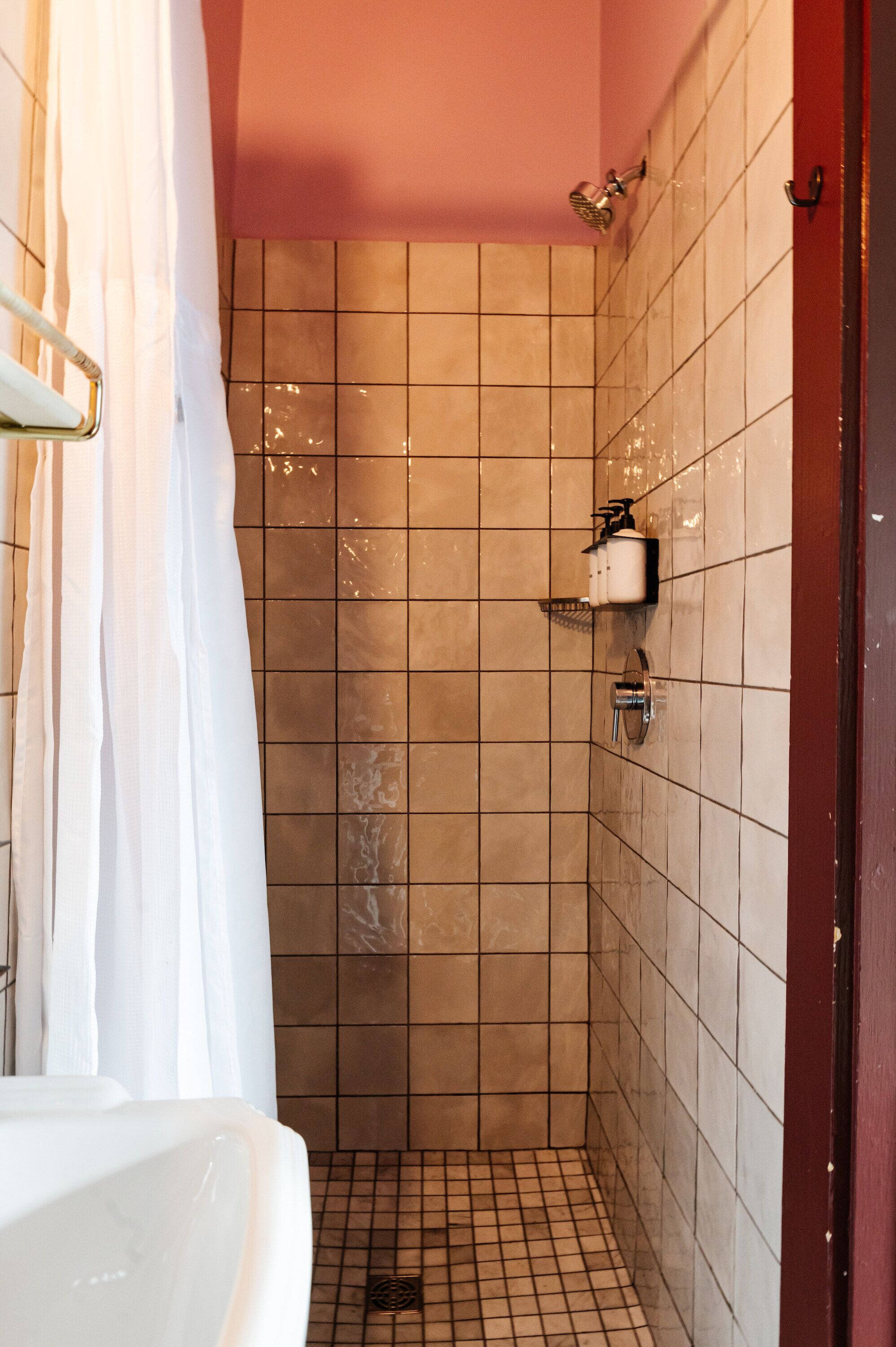 A small, tiled shower with a showerhead and a wall-mounted soap dispenser.