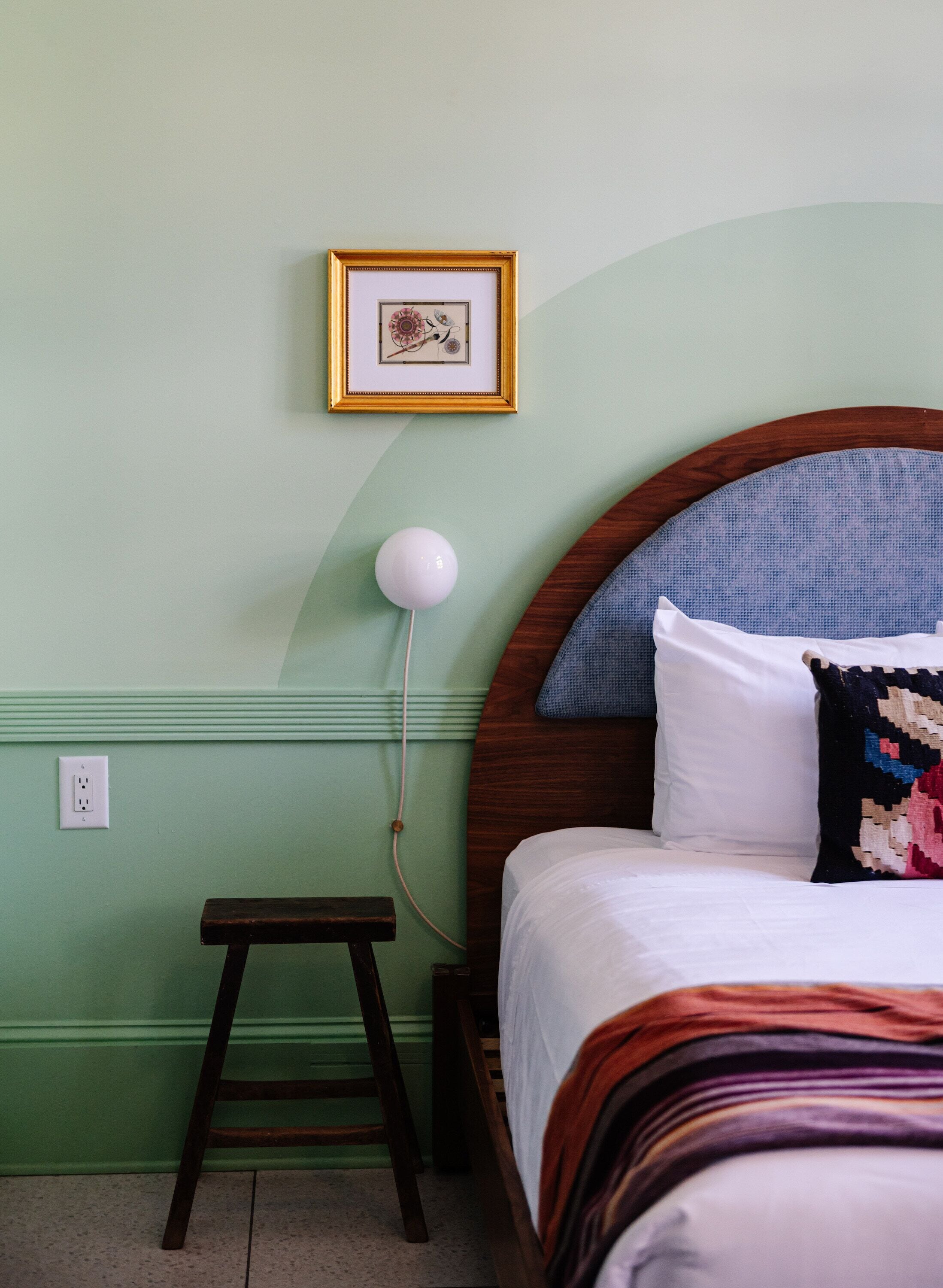 Een slaapkamer met een bed, een nachtkastje, een lamp, een lijst aan de muur en een stopcontact.