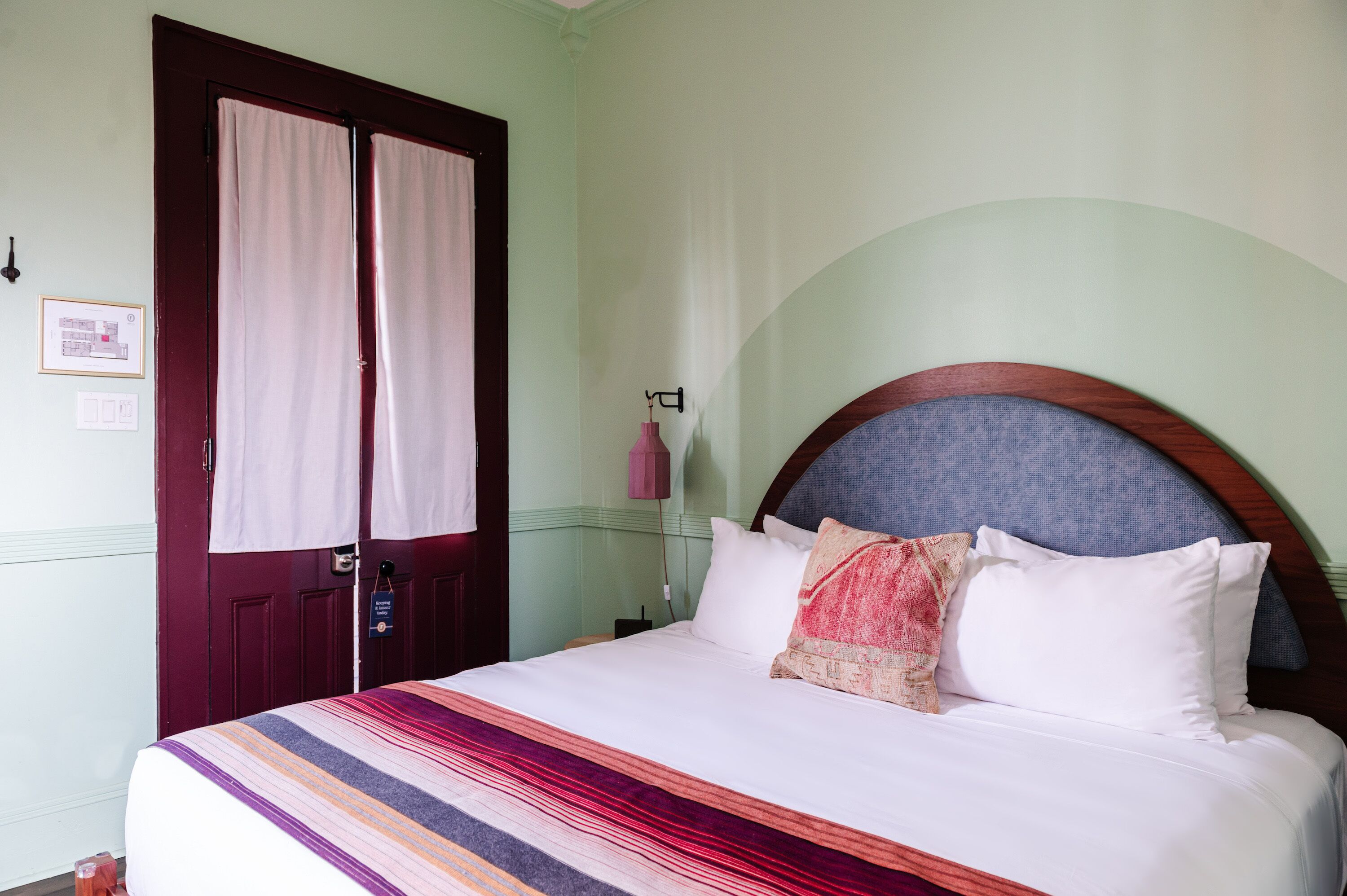 A bed with a striped bedspread, a headboard with a curved design, and a door with curtains.