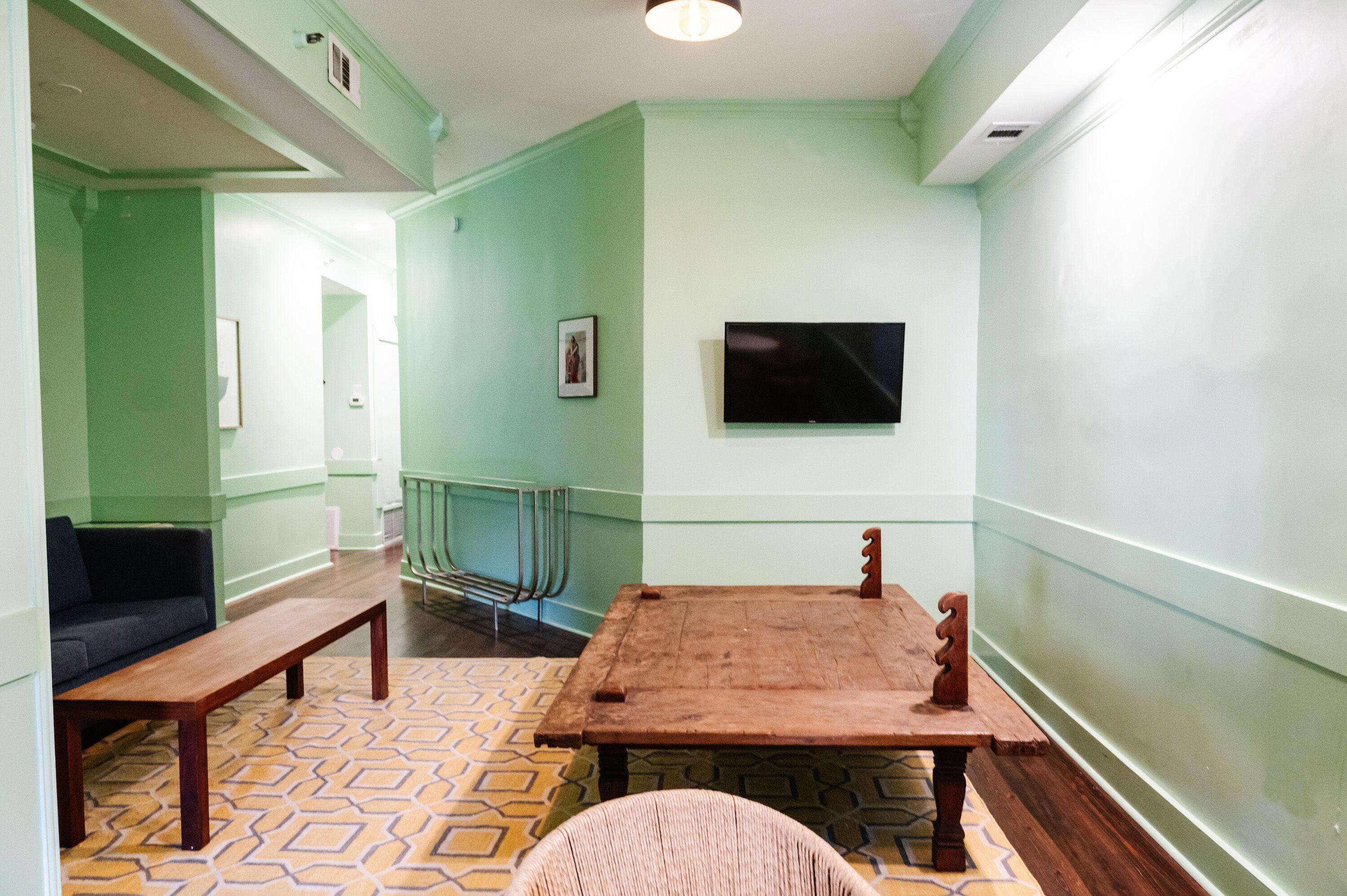 A room with a wooden table, a bench, a sofa, and a television on the wall.