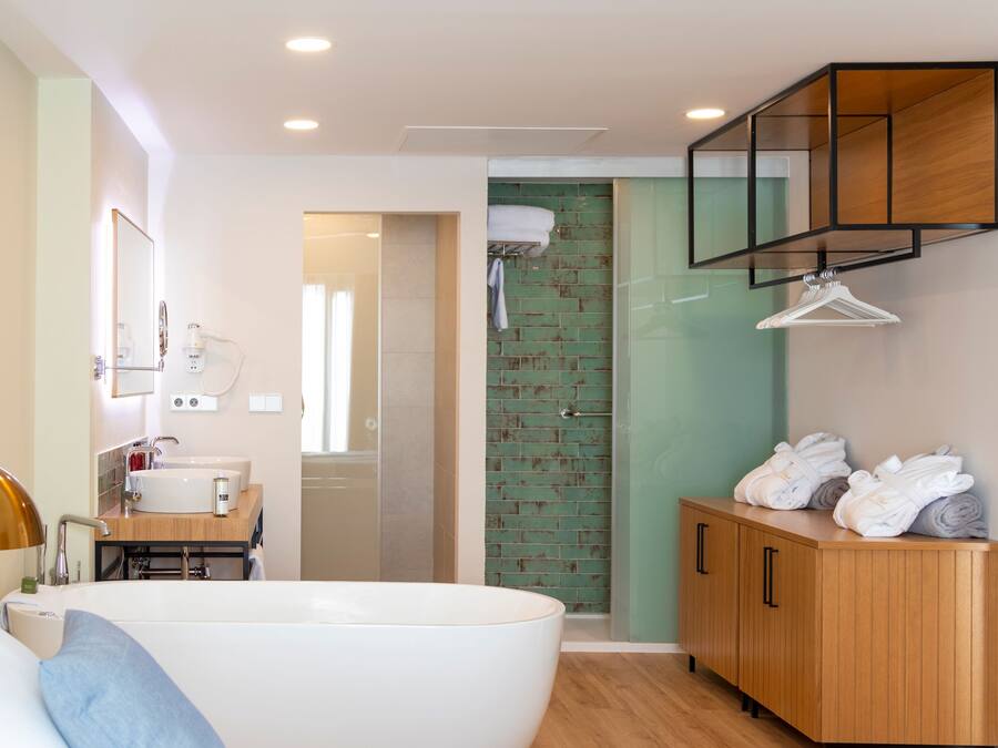 Un baño moderno con una bañera grande, un tocador de madera y una pared de ladrillo verde.