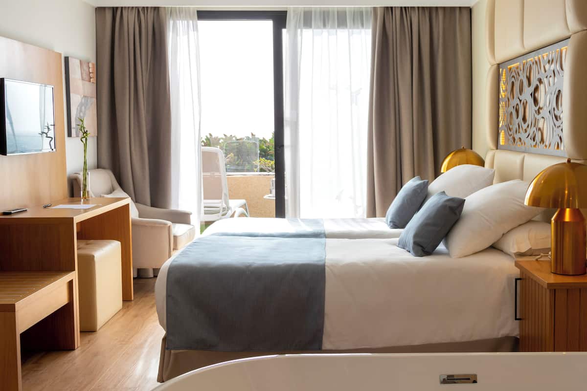 Quarto de hotel com cama, mesas de cabeceira, escrivaninha, cadeira e televisão.
