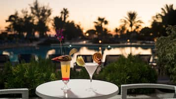 Zwei Cocktails auf einem Tisch, im Hintergrund Blick auf einen Pool.