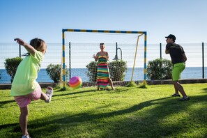 A grassy outdoor area with a goalpost, a person in a striped dress, and another in a cap. - Alexandre Grand Teguise Playa (Teguise)