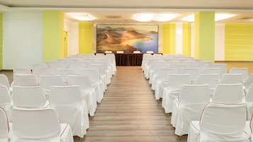Un salón de conferencias con filas de sillas blancas, un cuadro grande en la pared de fondo y suelo de madera.