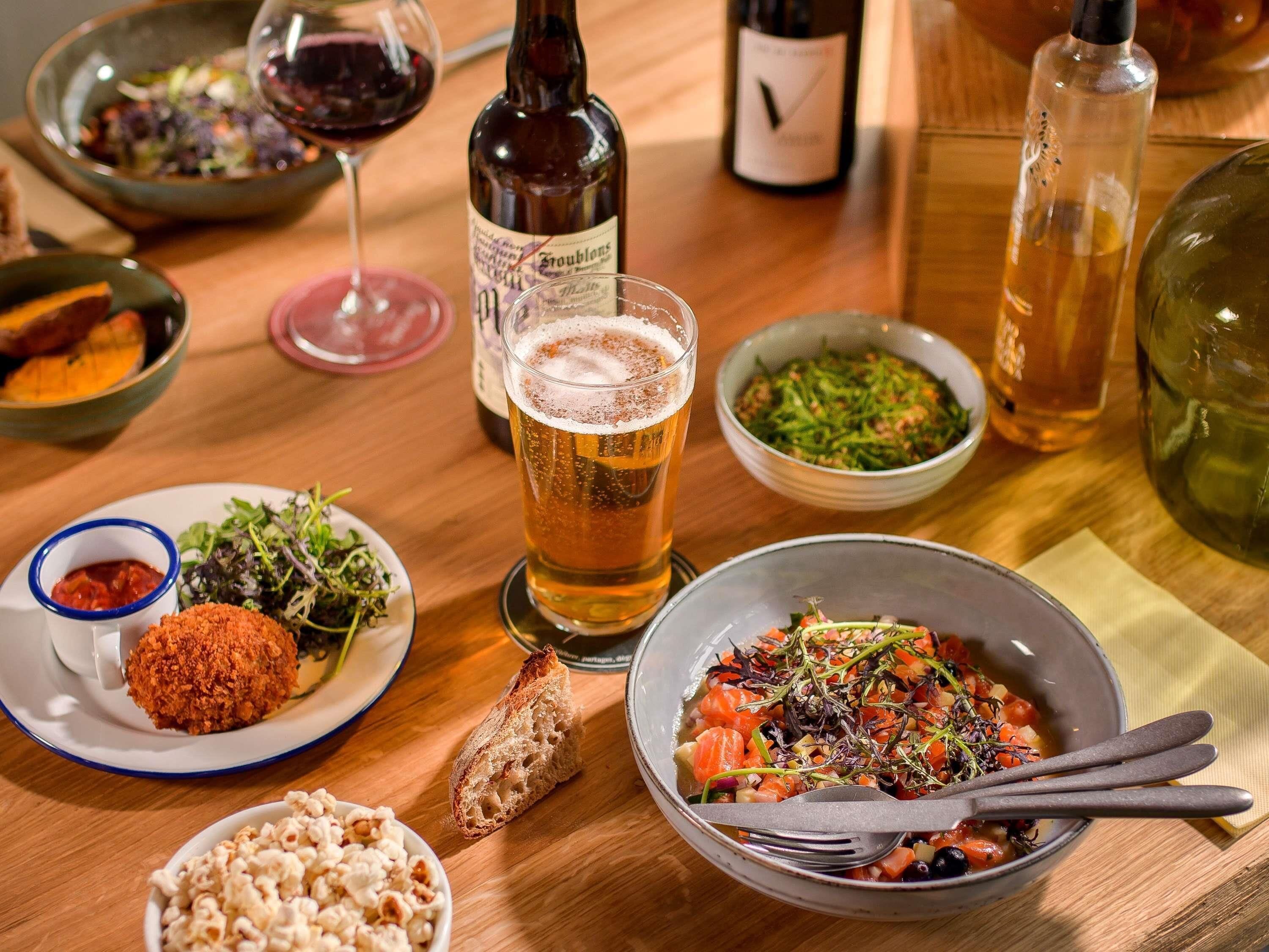 Een eettafel met diverse gerechten, een glas bier en flessen wijn.