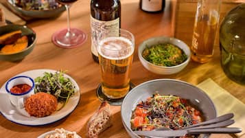 Een eettafel met diverse gerechten, een glas bier en flessen wijn.