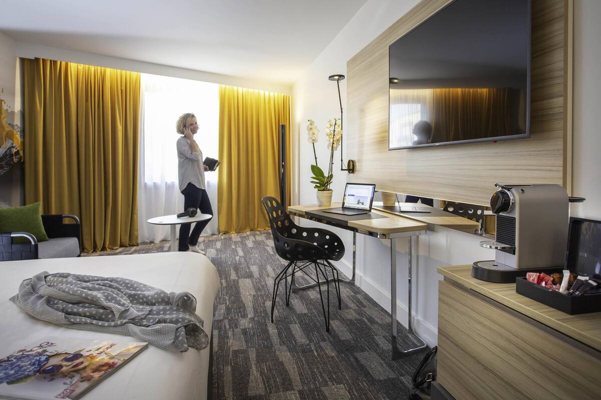 A hotel room with a bed, a desk, a TV, and a coffee machine.