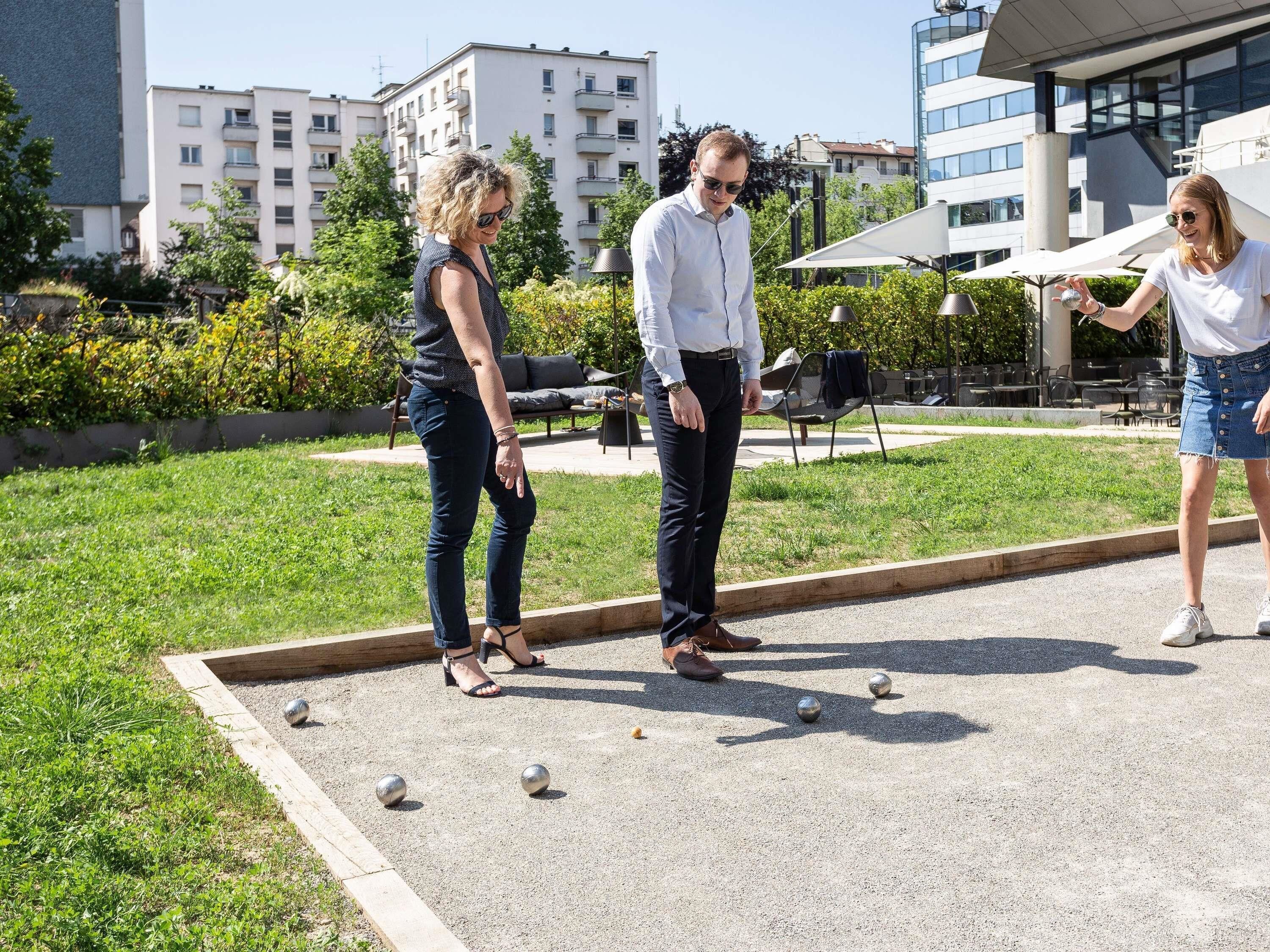 Een binnentuin met jeu de boules, zitplaatsen buiten en moderne gebouwen op de achtergrond.