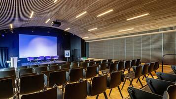 A conference room with rows of chairs, a stage with a large screen, and a wooden slatted ceiling.