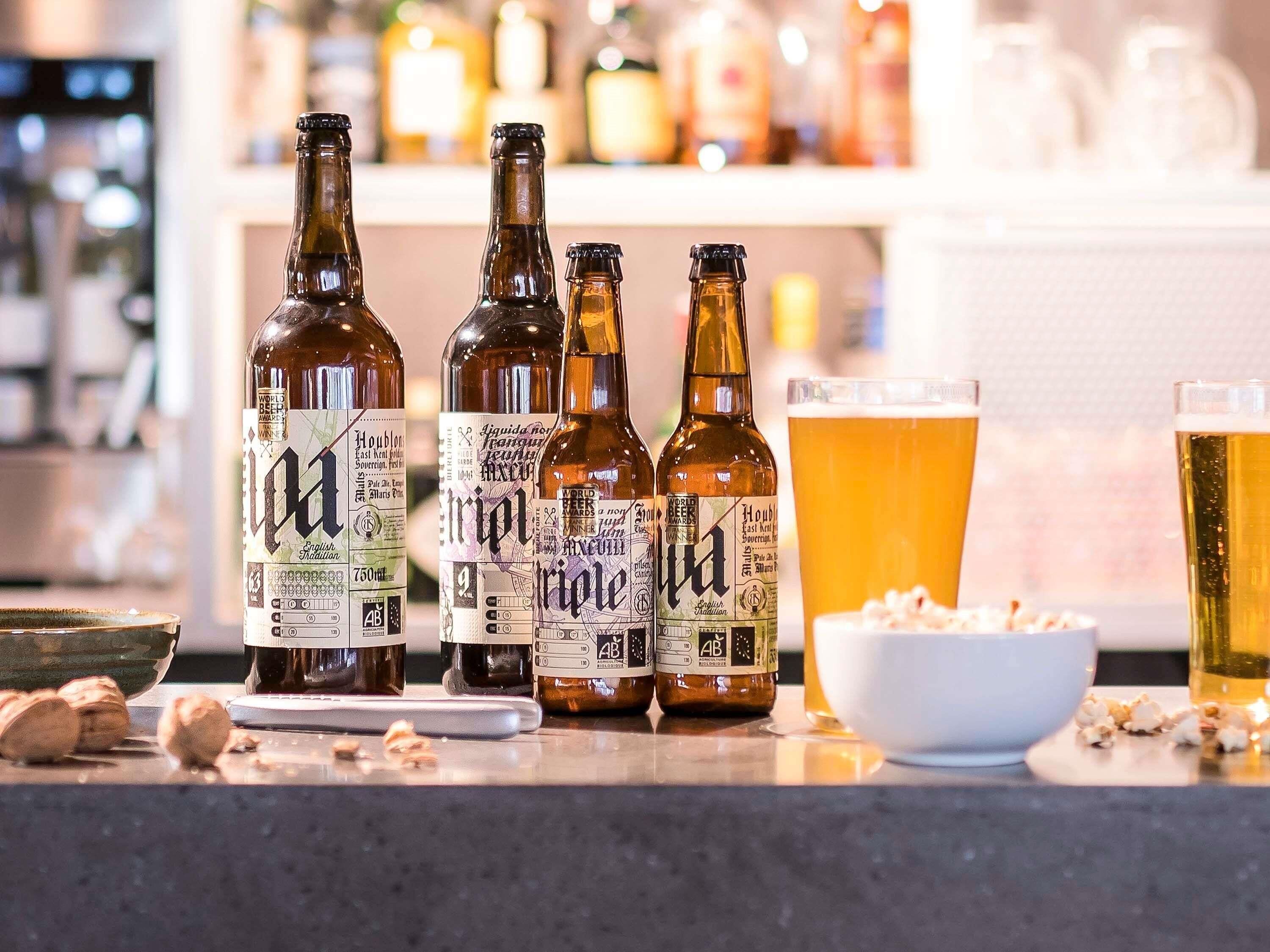 Three bottles of beer with labels, a glass of beer, and a bowl of popcorn on a counter.