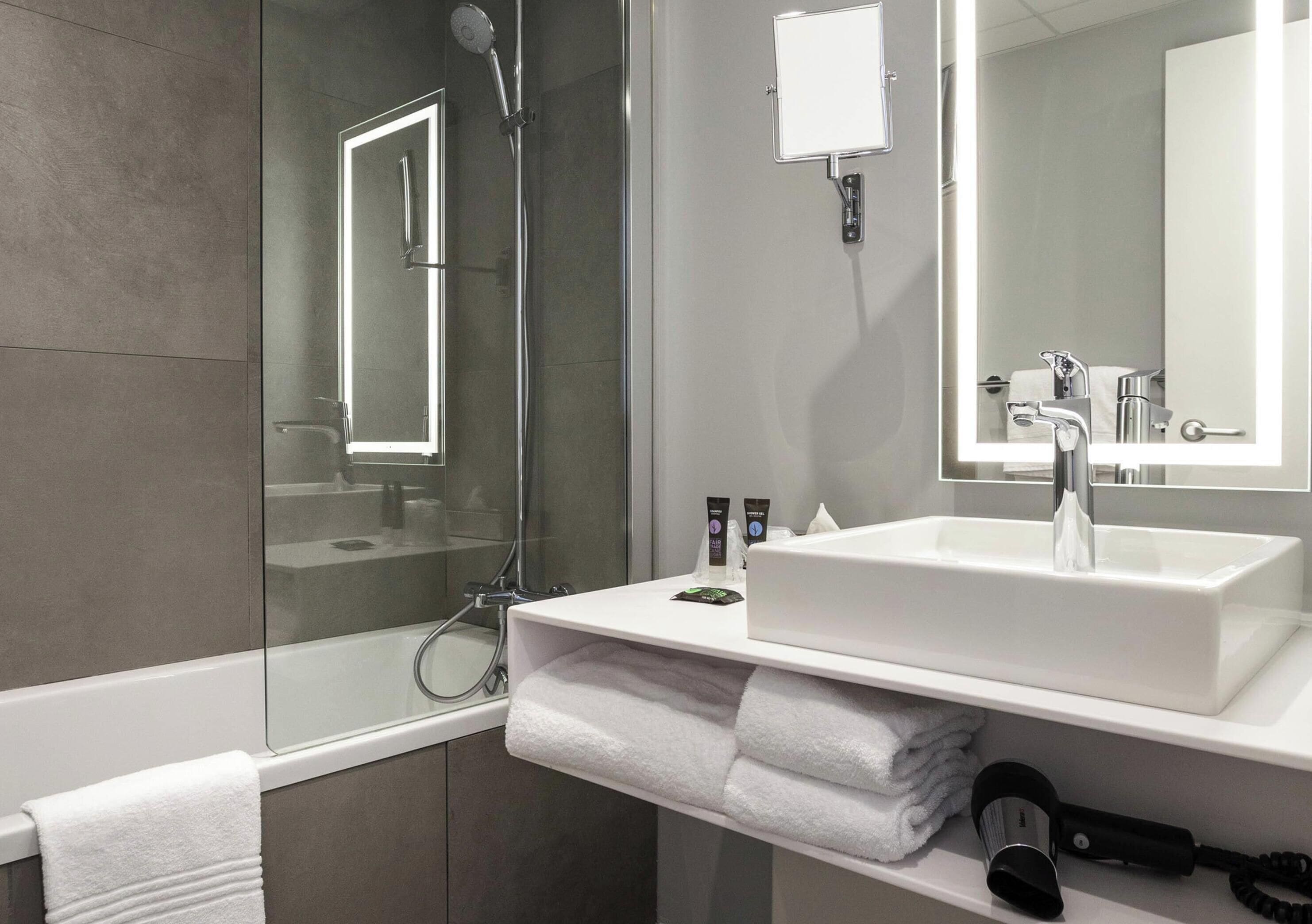 A modern bathroom with a glass-enclosed shower, a white sink with a mirror, and neatly folded towels.