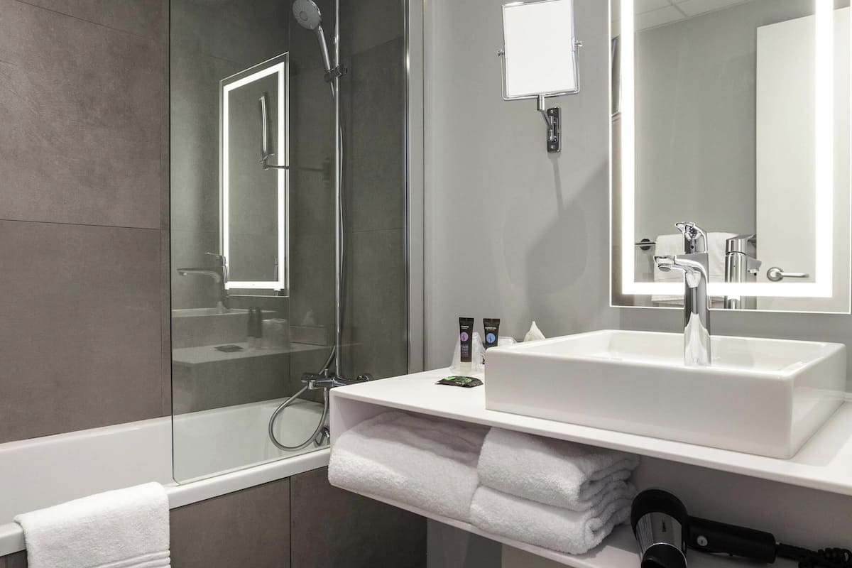 A modern bathroom with a glass-enclosed shower, a white sink with a mirror, and neatly folded towels.