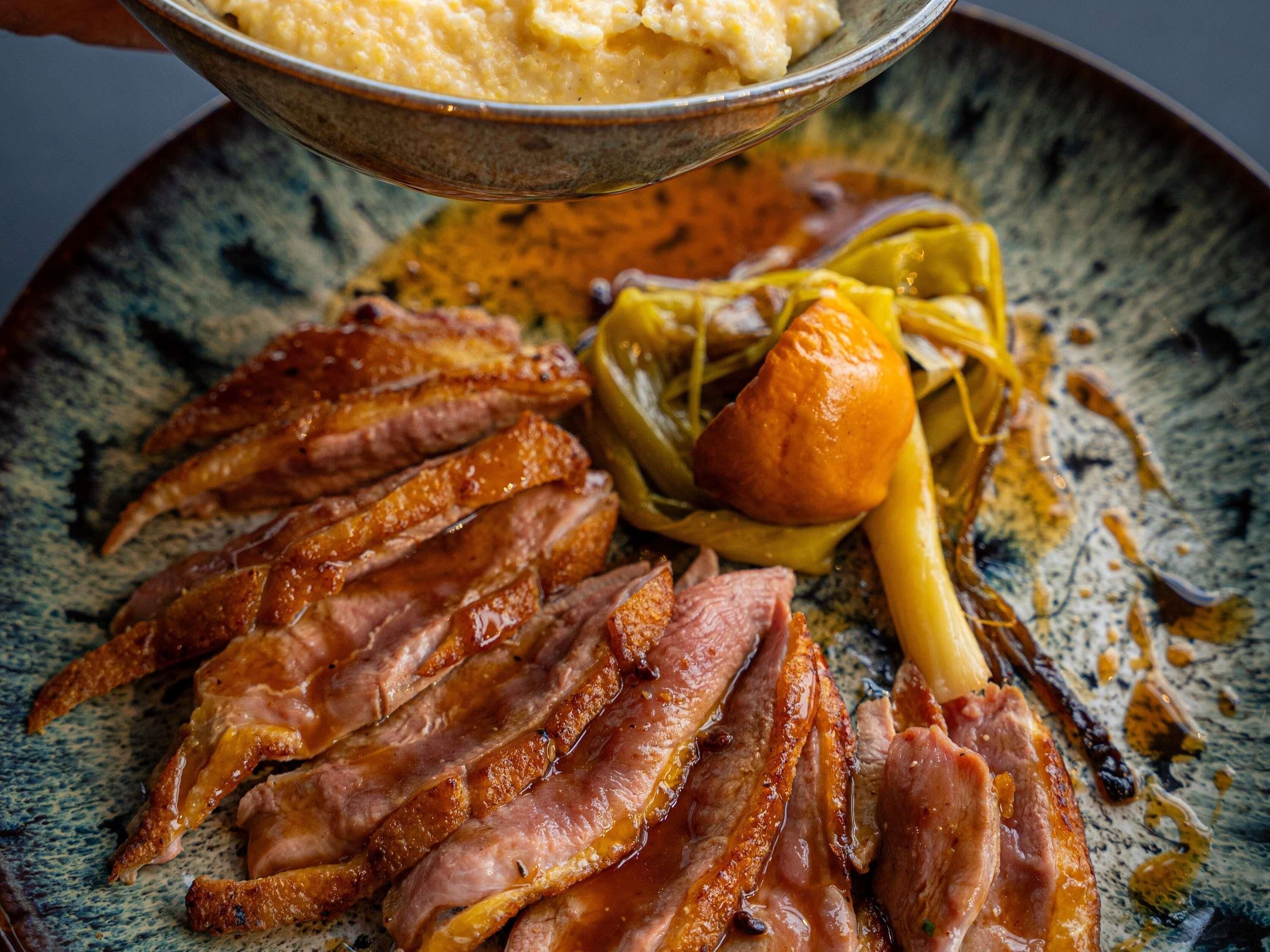 A plate with sliced meat, a bowl of mashed potatoes, and some vegetables.
